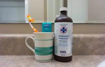 A bottle of hydrogen peroxide with oral care items in the washroom