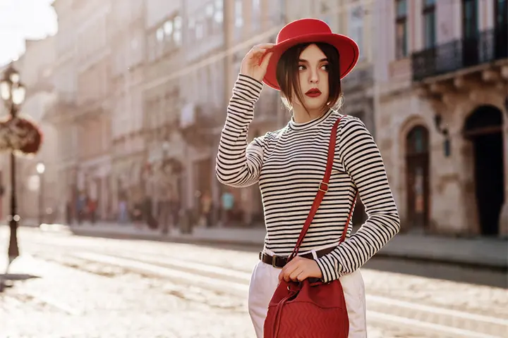 A woman in a white skirt and striped top with a red hat, bag, and lipstick