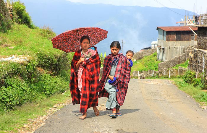 Two Khasi tribal woman can be seen walking with an umbrella and carrying a child on her back.