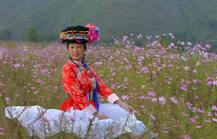A Mosuo tribal woman can be seen sitting in a flower field.
