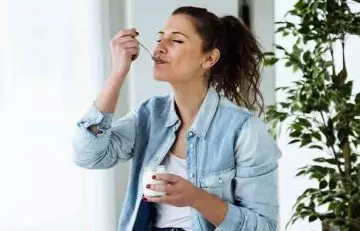 A woman is eating yogurt which is a probiotic.