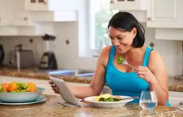 A woman is checking her calories intake and eating veggies.