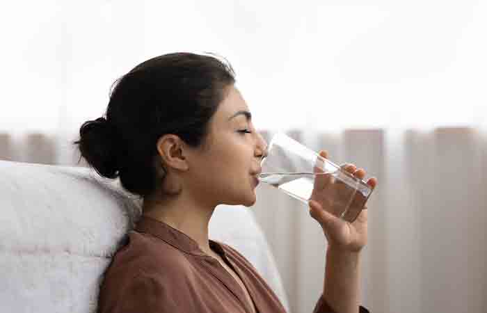 A woman is staying hydrated by drinking a glass of water.