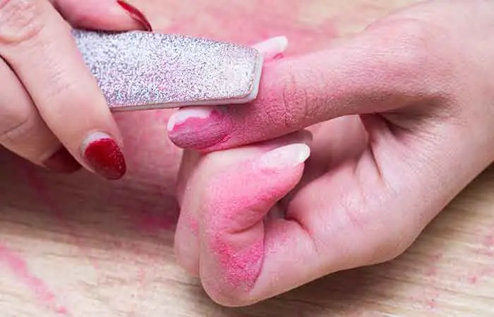 Close-up of hands of a woman buffing the surface of her acrylic nails for removal.