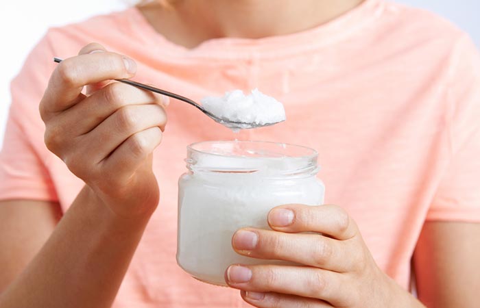 Woman taking out a tablespoon of coconut oil from jar