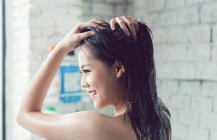 Woman washing off coconut oil from hair with lukewarm water