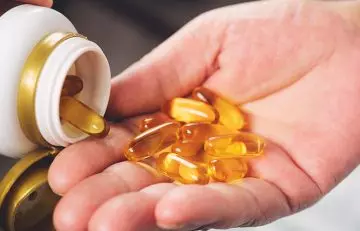 Person pouring fish oil capsules from the bottle into the hand