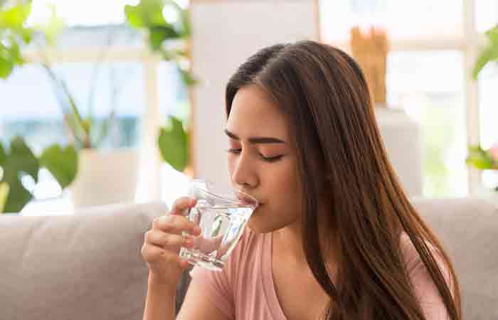 Woman drinking water for rehydration and hair health.