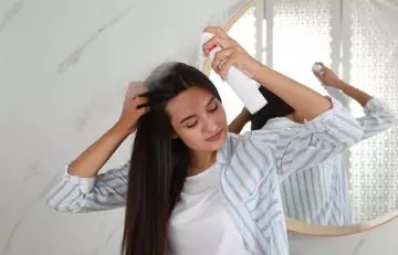A woman applying hair spray to tame flyaways