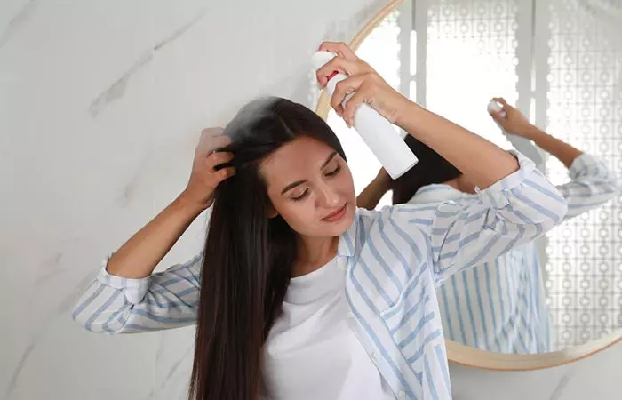 A woman applying hair spray to tame flyaways