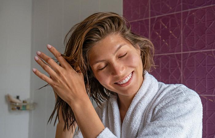 Woman applying cream-gel mixture on her towel dried hair