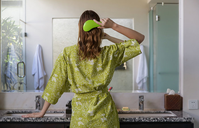 A woman combing her hair with a detangling brush in her bathroom