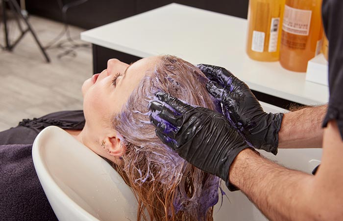 A stylist applies purple shampoo on a woman's hair