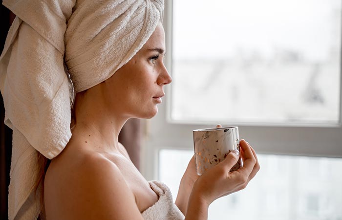A woman in bathrobes holding tea about to wash her hair