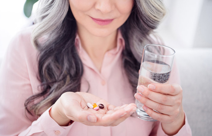 Gray haired woman taking vitamin supplements with water