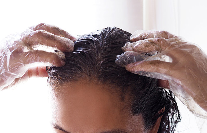 Closeup of a woman applying dye on her wet hair.