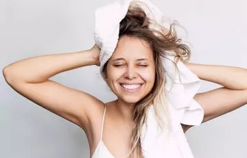 Woman drying her hair with microfiber towel before straightening it