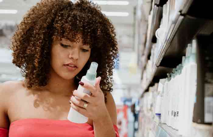 Curly haired woman checking the label on leave-in conditioner products in the mart