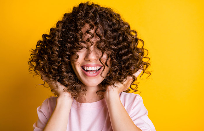 A happy woman touching her healthy curly hair.