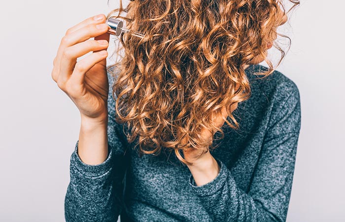 Woman applying serum on curly hair before silk pressing them
