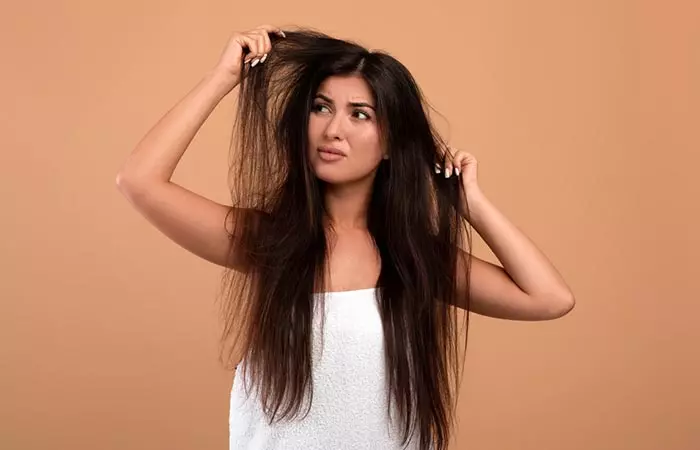 Woman looks upset with her dry and damaged hair as a result of chemicals used in salon hair spa treatments