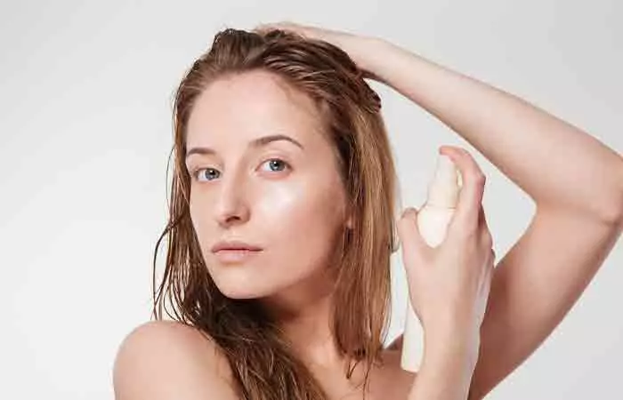 Woman spritzing coconut oil hairspray on damp hair
