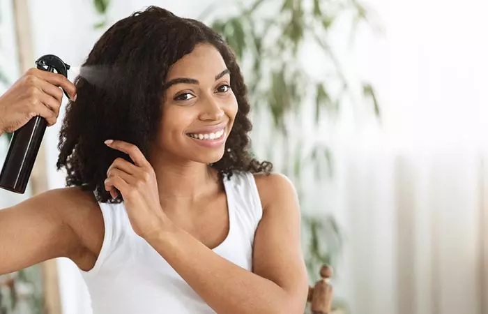 Woman applying hair spray to straighten her curly hair