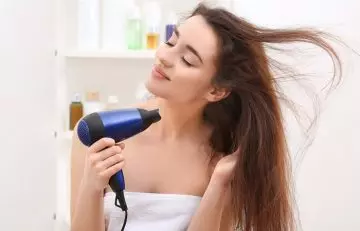 Woman blow drying hair on the cool setting to maintain hair health