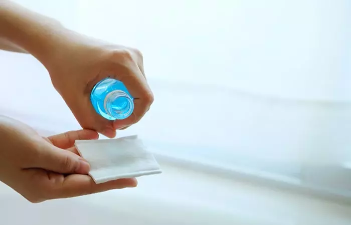 Person pouring rubbing alcohol over a cotton pad