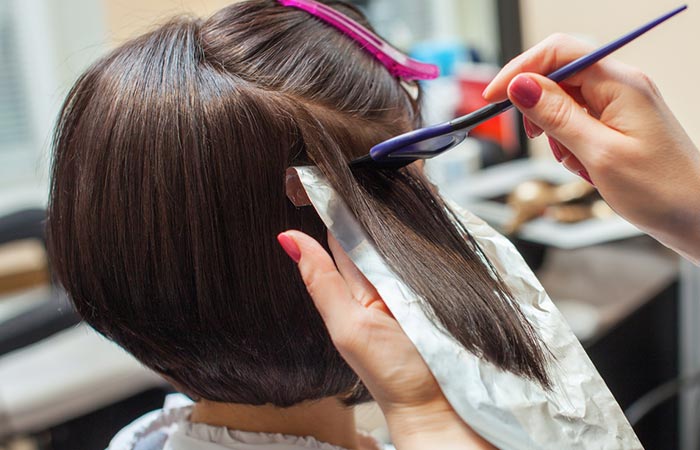 A salon professional applying a dark hair color to a woman's hair