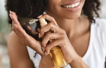 Woman using hair care product to repair heat-damaged curly hair