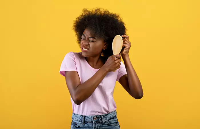 Woman having trouble combing her curly hair that has single strand knots and split ends