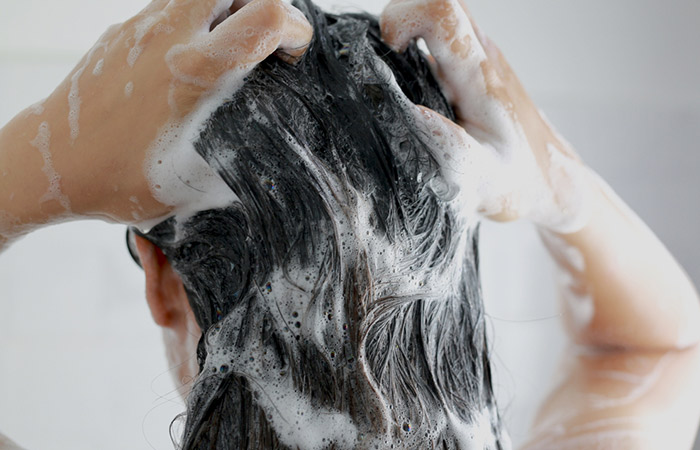 Woman applying tea tree oil shampoo to treat dandruff