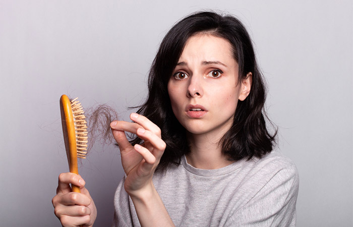 Woman looks worried looking at the hair loss on her hair brush