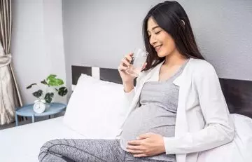A pregnant woman is drinking a glass full of water.