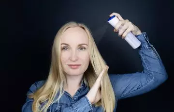 Woman applying dry shampoo on her fine hair to prep it for curling