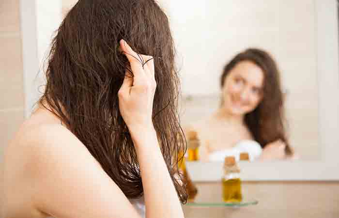 Smiling young woman applying oil to her hair in front of a mirror