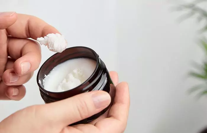 Woman scooping out hair butter from its container using her fingers