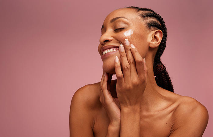 Smiling woman applying moisturizer on face