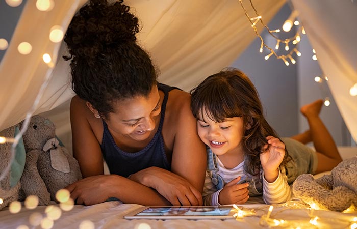 Mother and little girl enjoy videos on a tablet laying under an indoor makeshit tent
