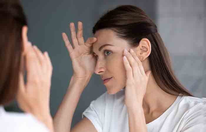 Washing face with cold water may benefit the woman examining wrinkles near her eyes