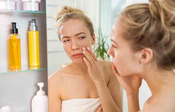 Washing face with cold water may benefit woman who is examining her puffy face