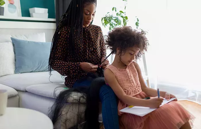 Woman braids daughter's hair while she does her homework