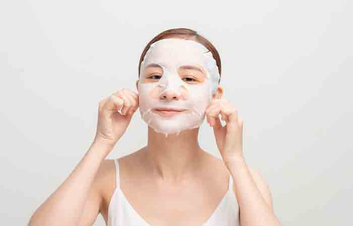 A woman applying a sheet mask as a part of her night skin care routine