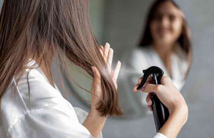Back view of woman using hair spray on her dull hair to restore its shine