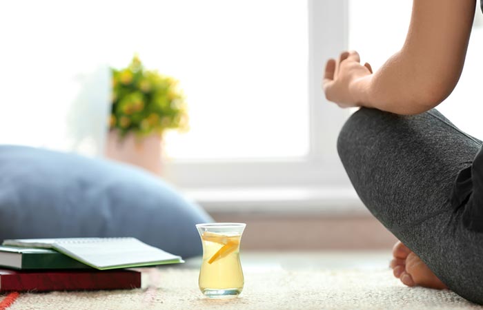 Person meditating beside a cup of lemon tea as part of their detox routine