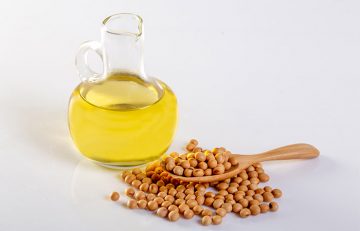 A jar of soybean oil and a wooden spoon with soybeans