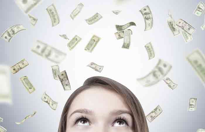 Top half of a woman's face who is looking up as dollar bills fall from above