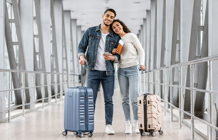 A couple on their way to a trip pose at the airport with their luggage
