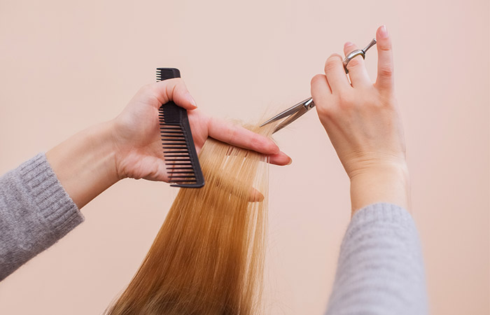 Person trimming blonde hair with scissors